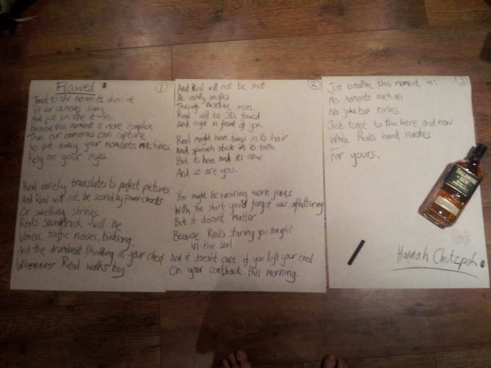 Three sheets of paper with handwriting on them, with a bottle of whisky and a piece of charcoal on the third sheet of paper