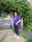 Hannah wearing her purple 'shine' marathon t-shirt, standing in front of some vines wearing trainers and black leggings